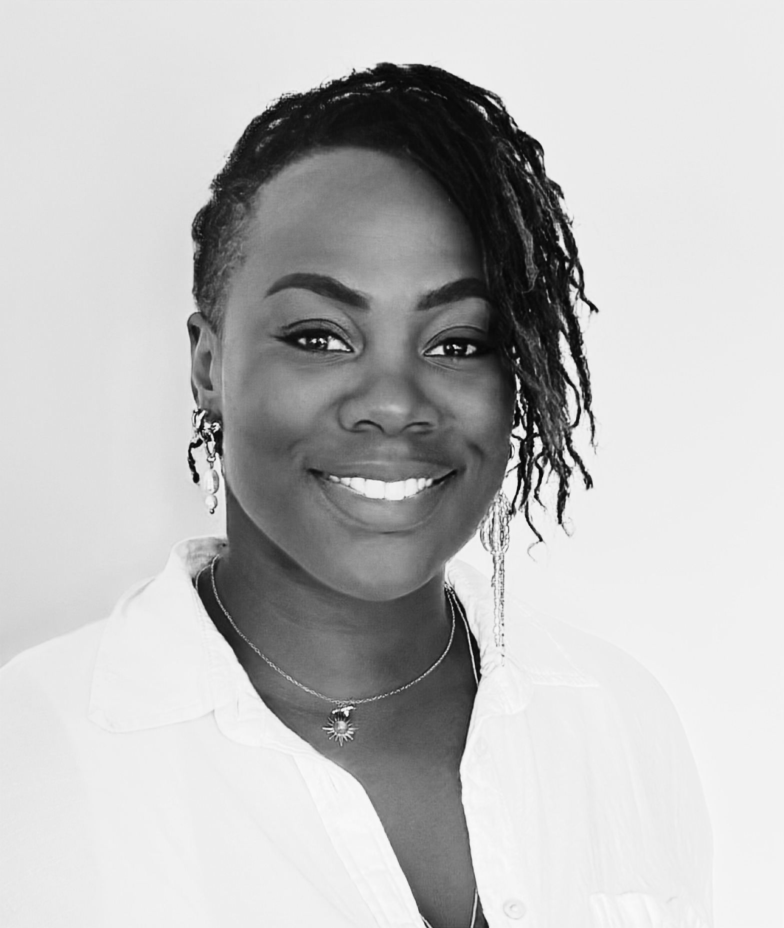 Florence Sedaminou, xwedu Senior Lead Mentor for intercultural and organisational transformation, in a black and white portrait with braided hair, a white shirt, and a sun pendant necklace